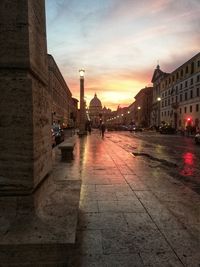 Wet street amidst buildings in city against sky