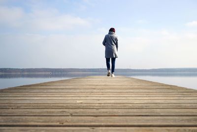 Rear view of woman walking on pier over lake against sky