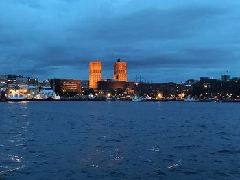 Illuminated buildings by river against sky at dusk