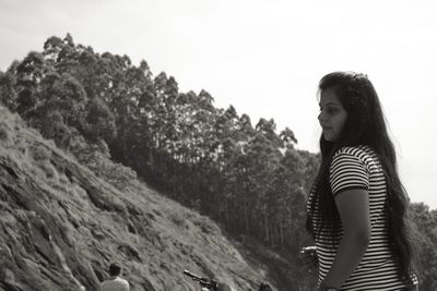 Side view of smiling young woman standing against sky