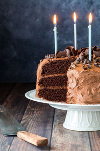 A triple layered chocolate cake with lit candles, against a dark background.