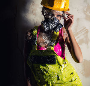 Young woman in coveralls wearing gas mask against wall