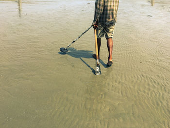 Low section of man holding tools at beach