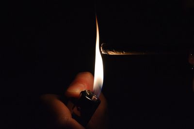 Close-up of cropped hand lighting cigarette in darkroom