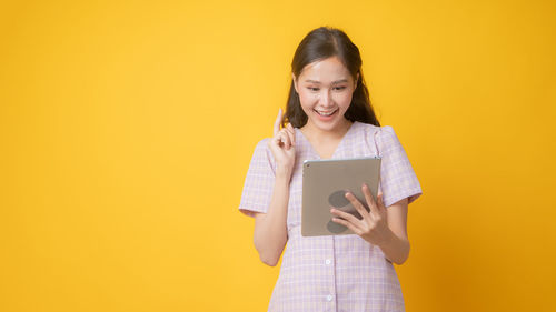 Portrait of a smiling young woman standing against yellow background