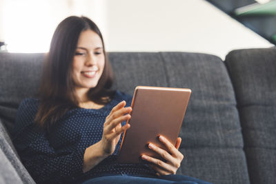 Young woman using digital tablet while sitting on sofa at home