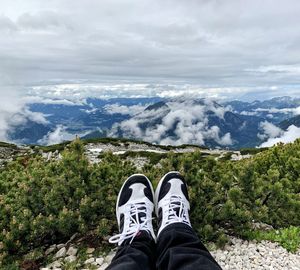 Low section of person sitting on mountain against sky