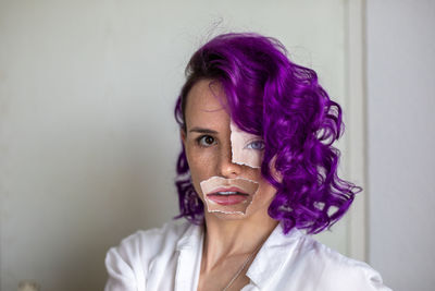 Portrait of woman wearing paper on face standing against wall at home