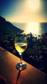 Close-up of wineglass on table against sea during sunset