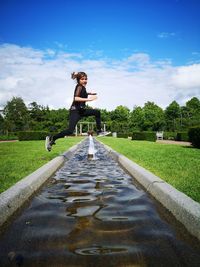 Girl jumping over fountain against sky