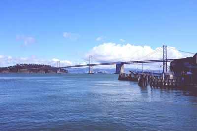 Suspension bridge over river against cloudy sky