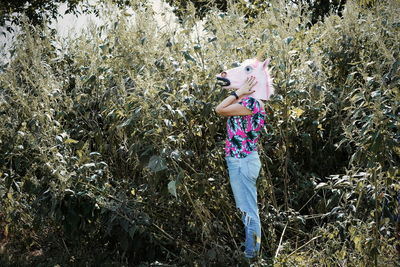 Full length of woman wearing unicorn mask while standing amidst plants