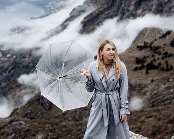 Portrait of young woman standing on rocks with umbrella 