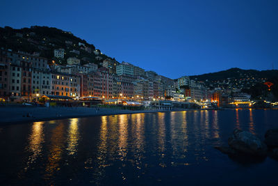 Illuminated buildings by lake against sky at night
