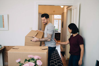 Woman standing by man carrying cardboard box in living room