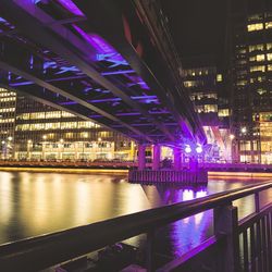 Low angle view of illuminated bridge over river against buildings at night in city