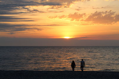 Silhouette men standing on beach against sky during sunset