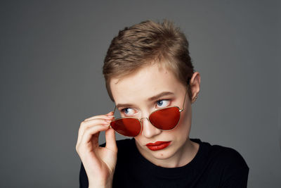 Portrait of young woman holding sunglasses against gray background