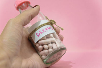 Close-up of hand holding pill bottle with dreams label against colored background