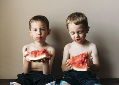 Portrait of boy eating watermelon with brother at home