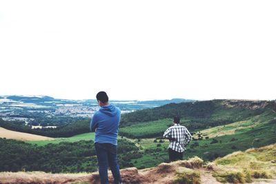 Rear view of men standing on mountain against clear sky