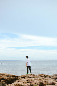 Rear view of woman standing on rock by sea against sky