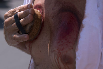 Midsection of man with injured body holding sharp equipment during religious event