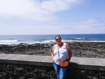 Woman standing by retaining wall against sea at beach