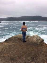 Rear view of man standing at beach against sky