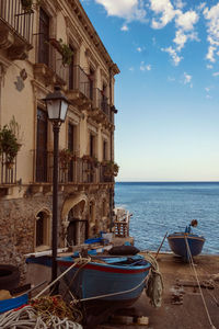 Boats moored on sea by buildings against sky