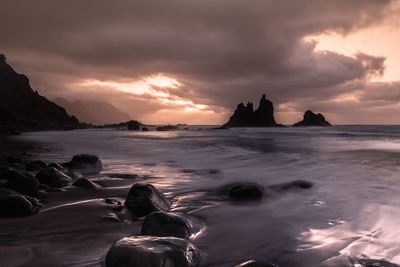 Long exposure of beach onnorth coast of canary island of tenerife at sunset with dramatic clouds .