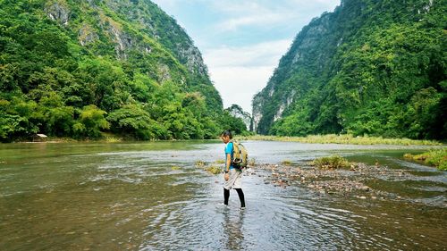 Hiker walking in river by mountains