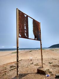 Abandoned wooden post on beach against clear blue sky