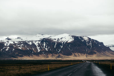 Road leading towards mountain against cloudy sky during winter