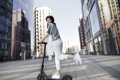 Woman with e-scooter and helmet, modern office buildings in the background