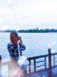 Rear view of woman photographing by sea against sky