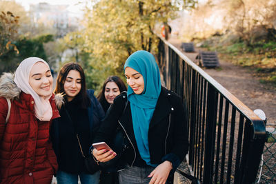 High angle view of young woman sharing smart phone with multi-ethnic friends on staircase in city