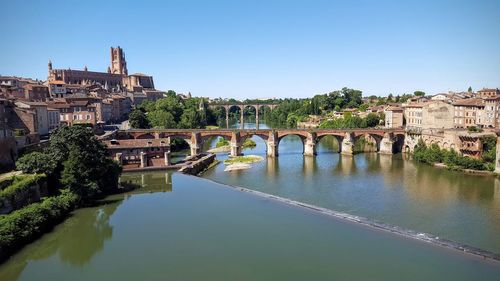 Bridge over river in city against clear blue sky