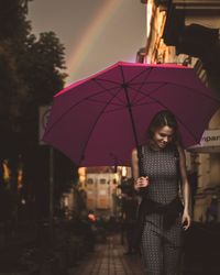 Woman with umbrella walking in city during sunset