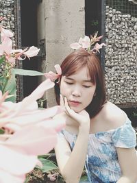 Beautiful woman holding flower while standing by potted plant