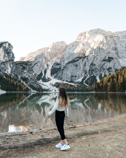 Rear view of woman standing by lake against mountains