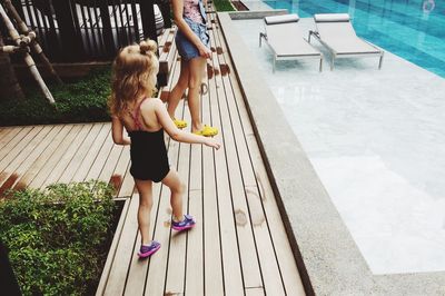 Rear view of girl standing by mother at poolside