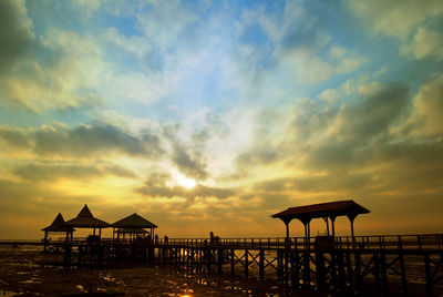 Silhouette parasols on beach against sky during sunset