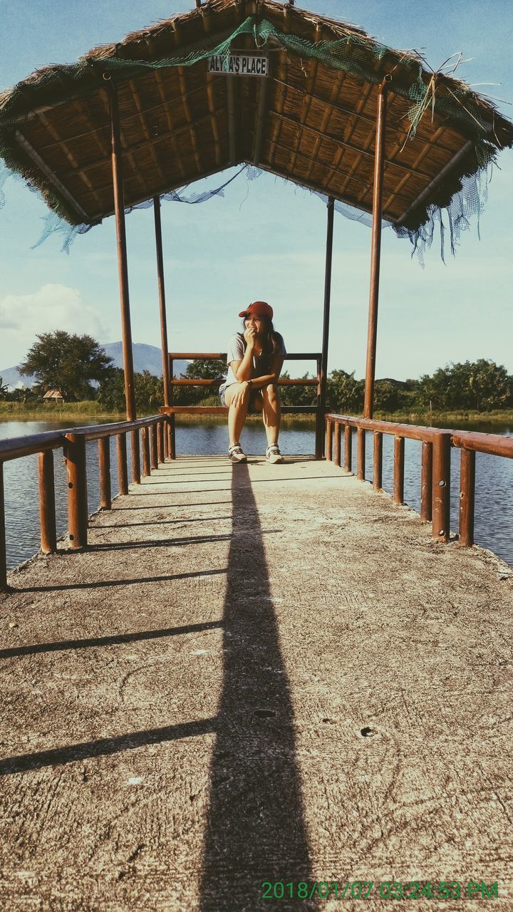 PORTRAIT OF WOMAN STANDING ON RAILING AGAINST SKY