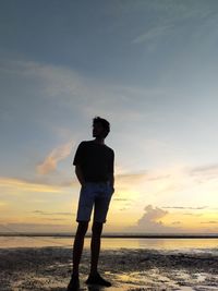 Man standing on beach against sky during sunset