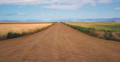 Dirt road amidst field against sky