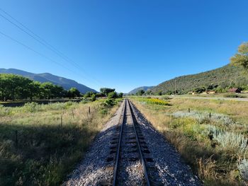 Railroad track amidst field against clear blue sky