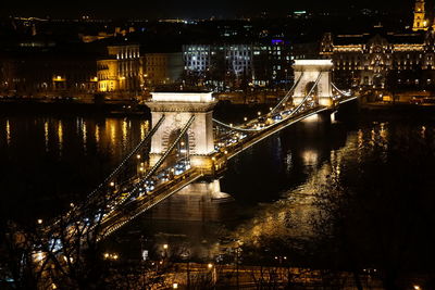 Illuminated bridge over river in city at night