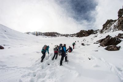 Low angle view of people hiking on snow covered mountains against sky