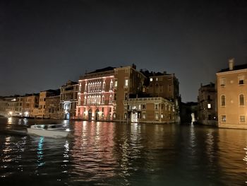 Buildings by lake against sky in city at night